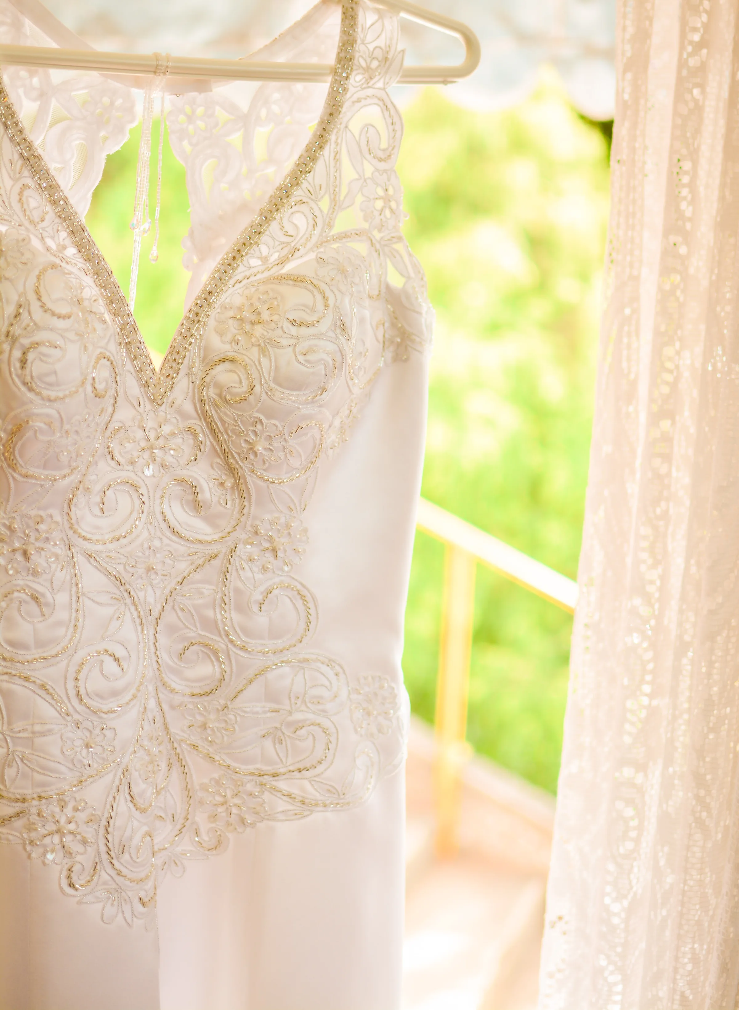 Vestido bordado com pedrarias pendurado em cabide junto à janela com cortina