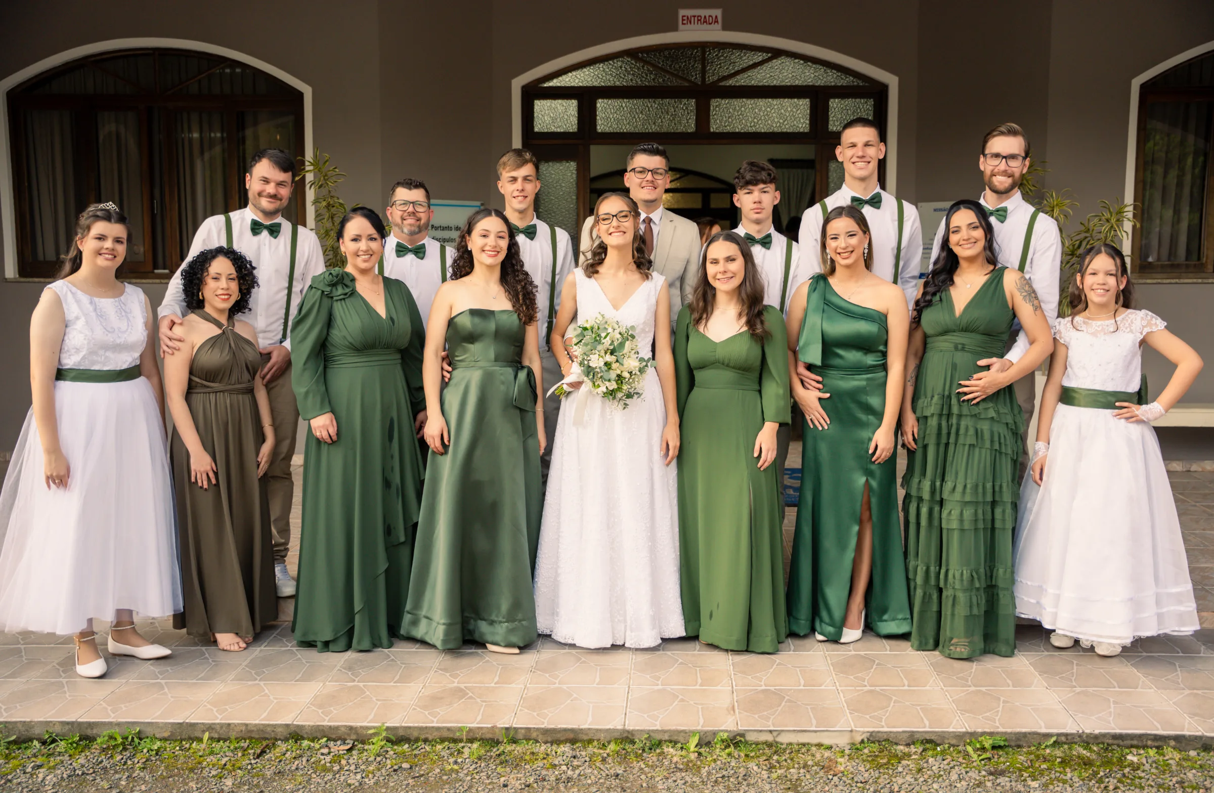 Casal com padrinhos de verde e suspensórios posando na entrada do salão