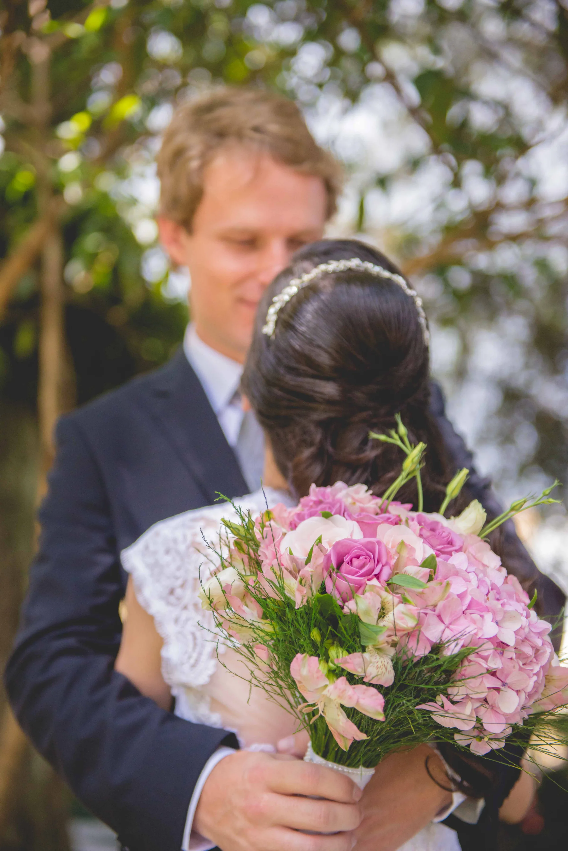 Buquê de hortênsias e rosas em foco, casal abraçado desfocado ao fundo