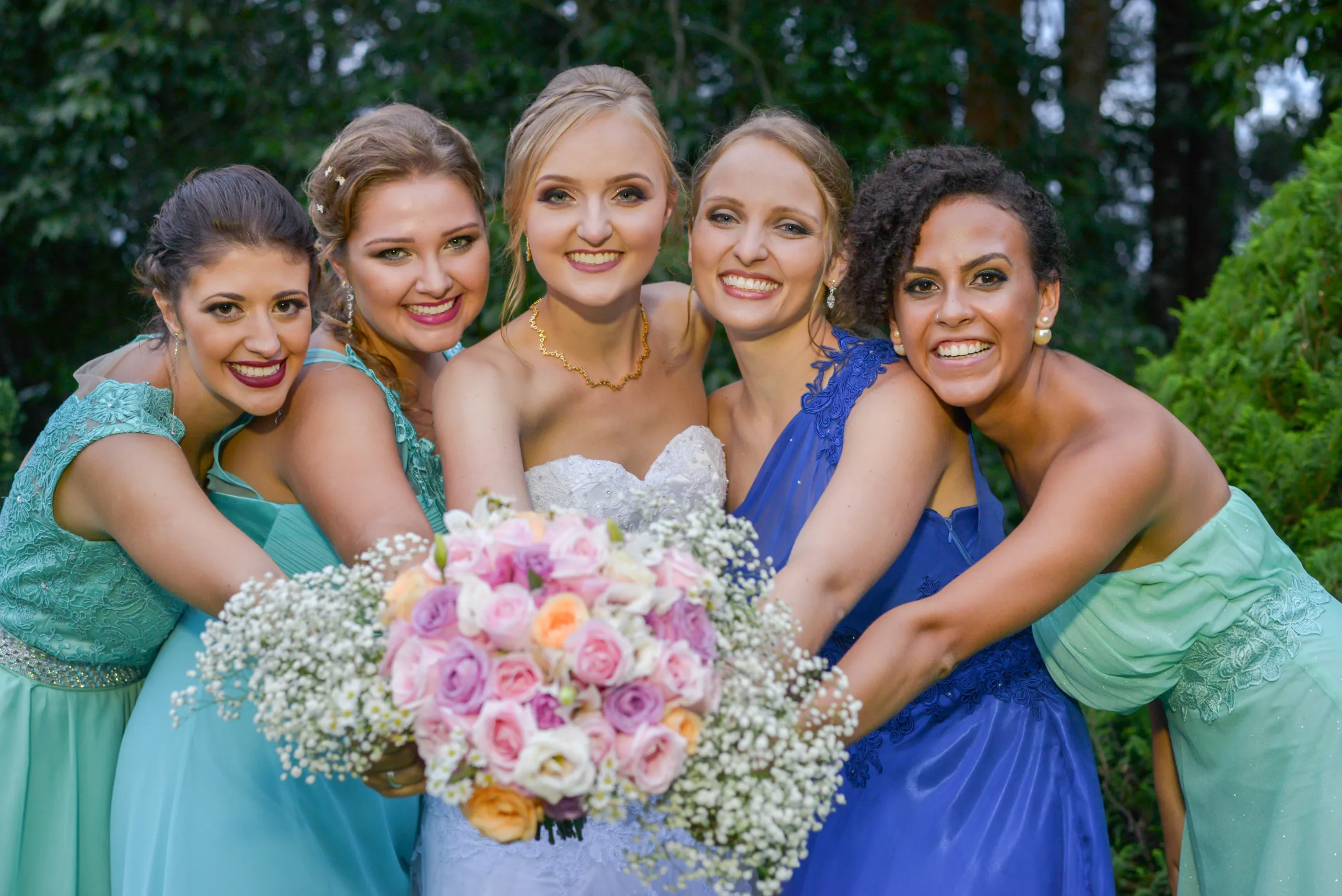 Cinco mulheres abraçadas em volta da noiva com buquê de rosas e gipsofilas
