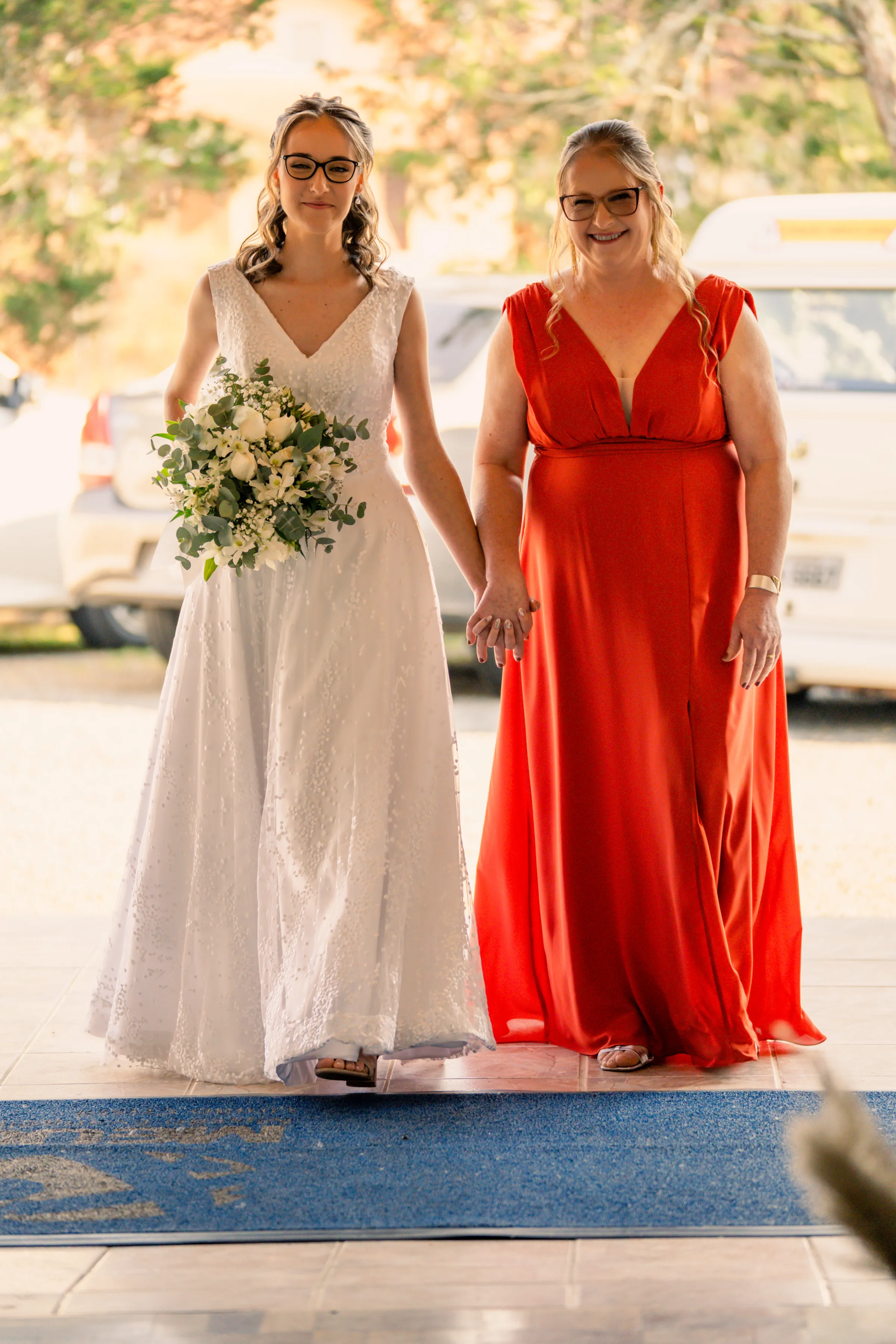 Noiva de mãos dadas com mulher de vestido vermelho a caminho da cerimônia