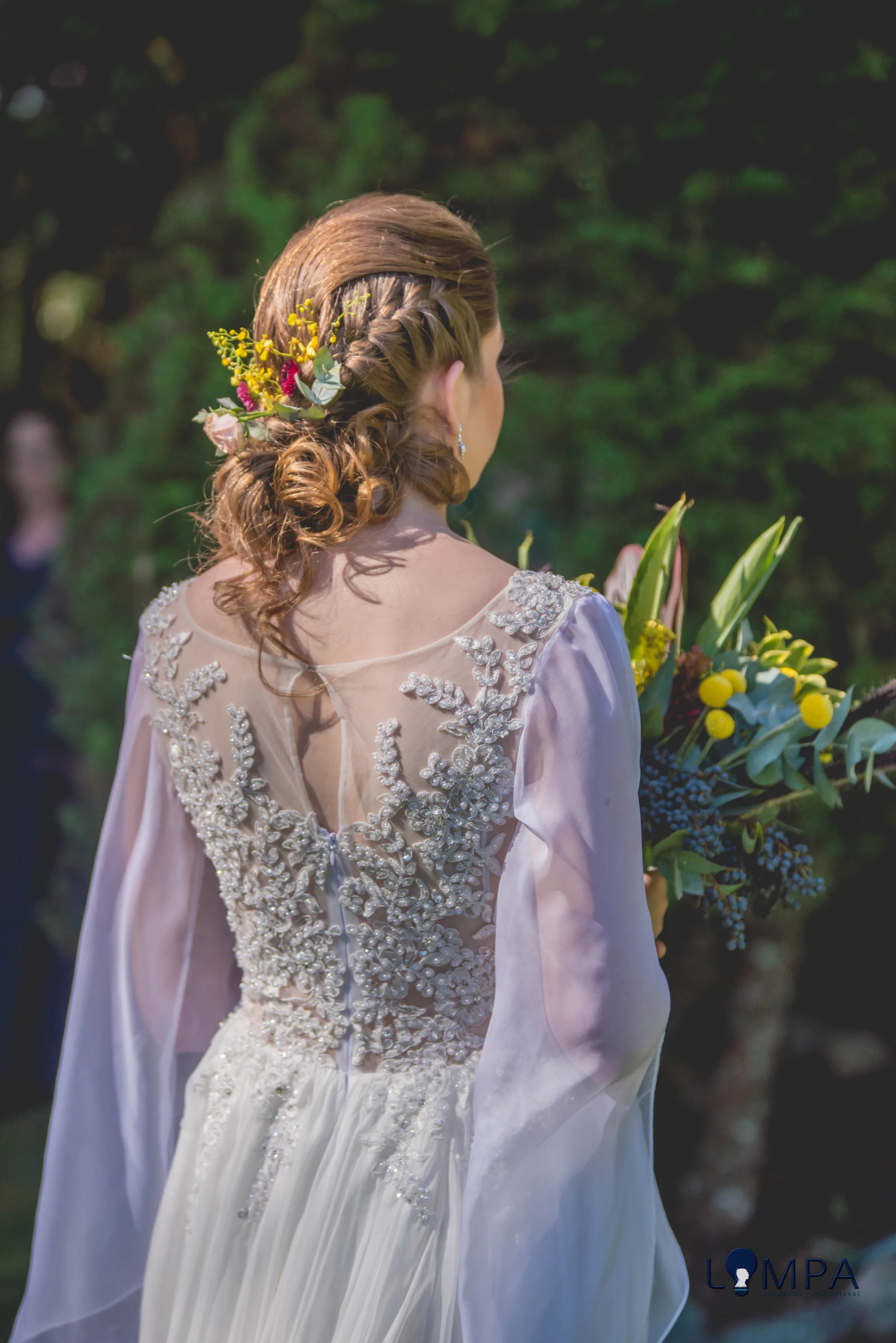 Costas do vestido com pedrarias e trança com flores amarelas no coque
