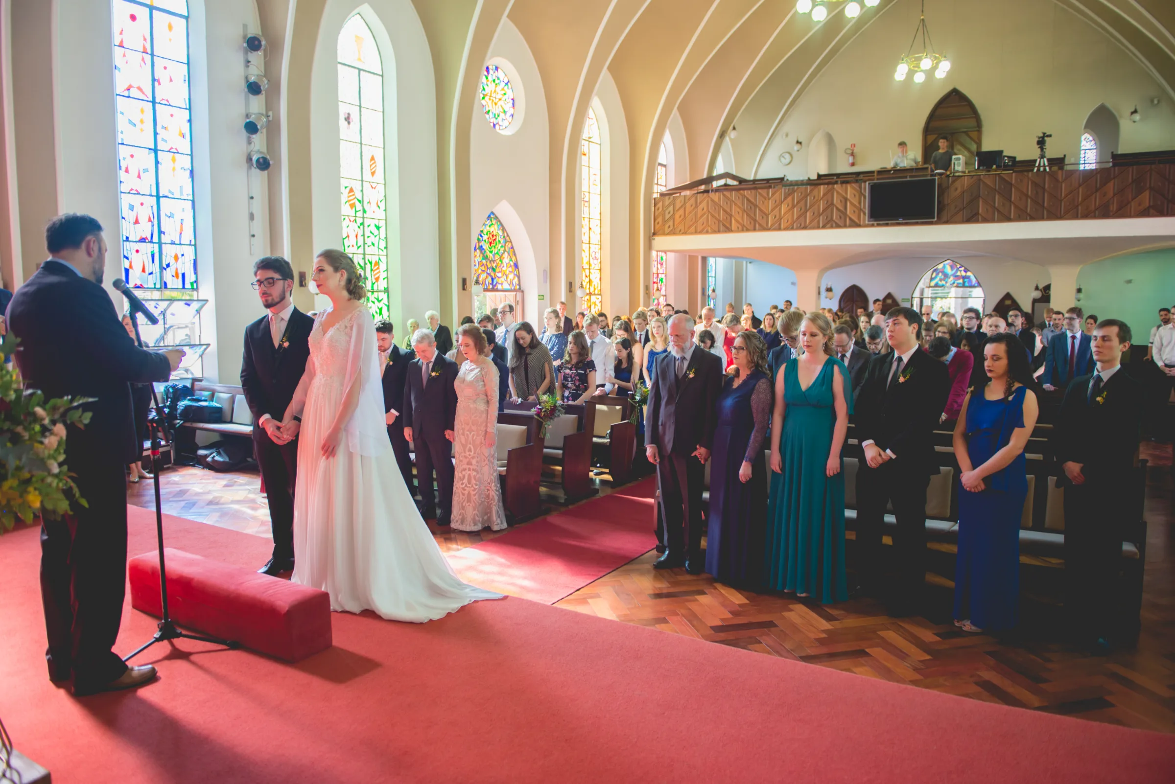 Celebrante fala ao casal diante da igreja lotada com vitrais coloridos