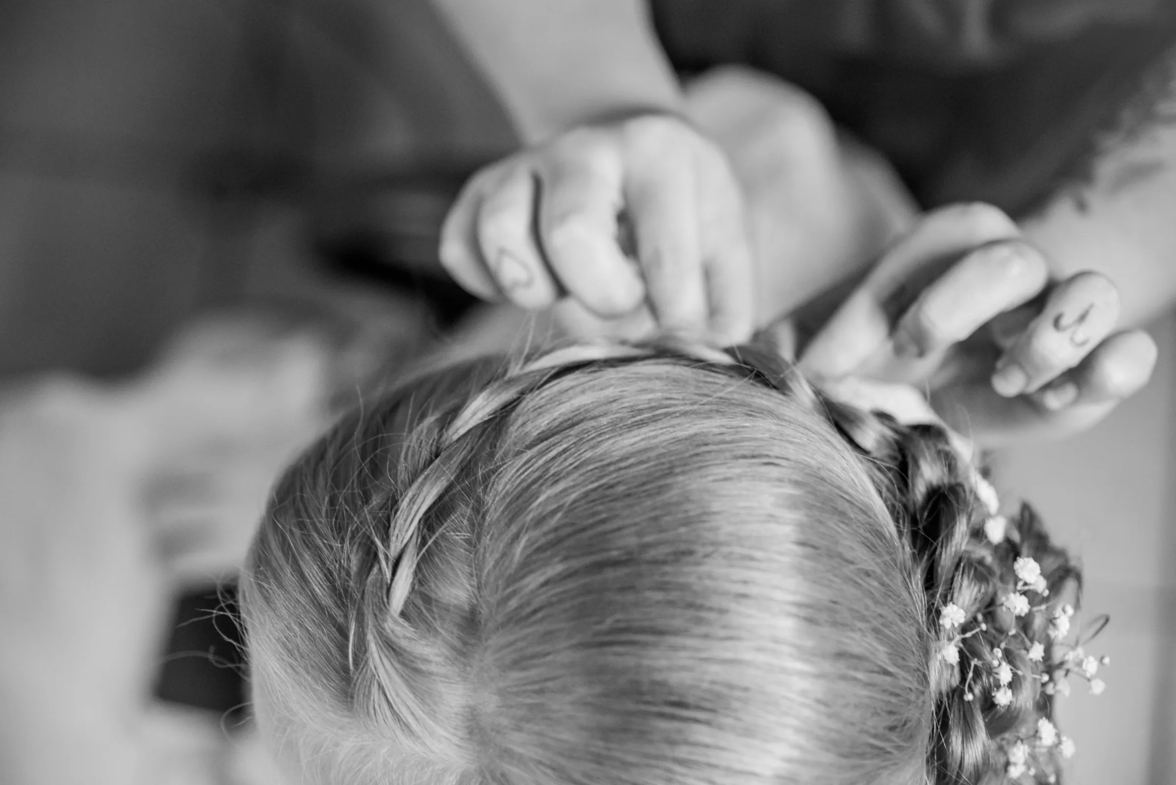 Mãos da cabeleireira finalizando trança com flores miúdas no penteado da noiva