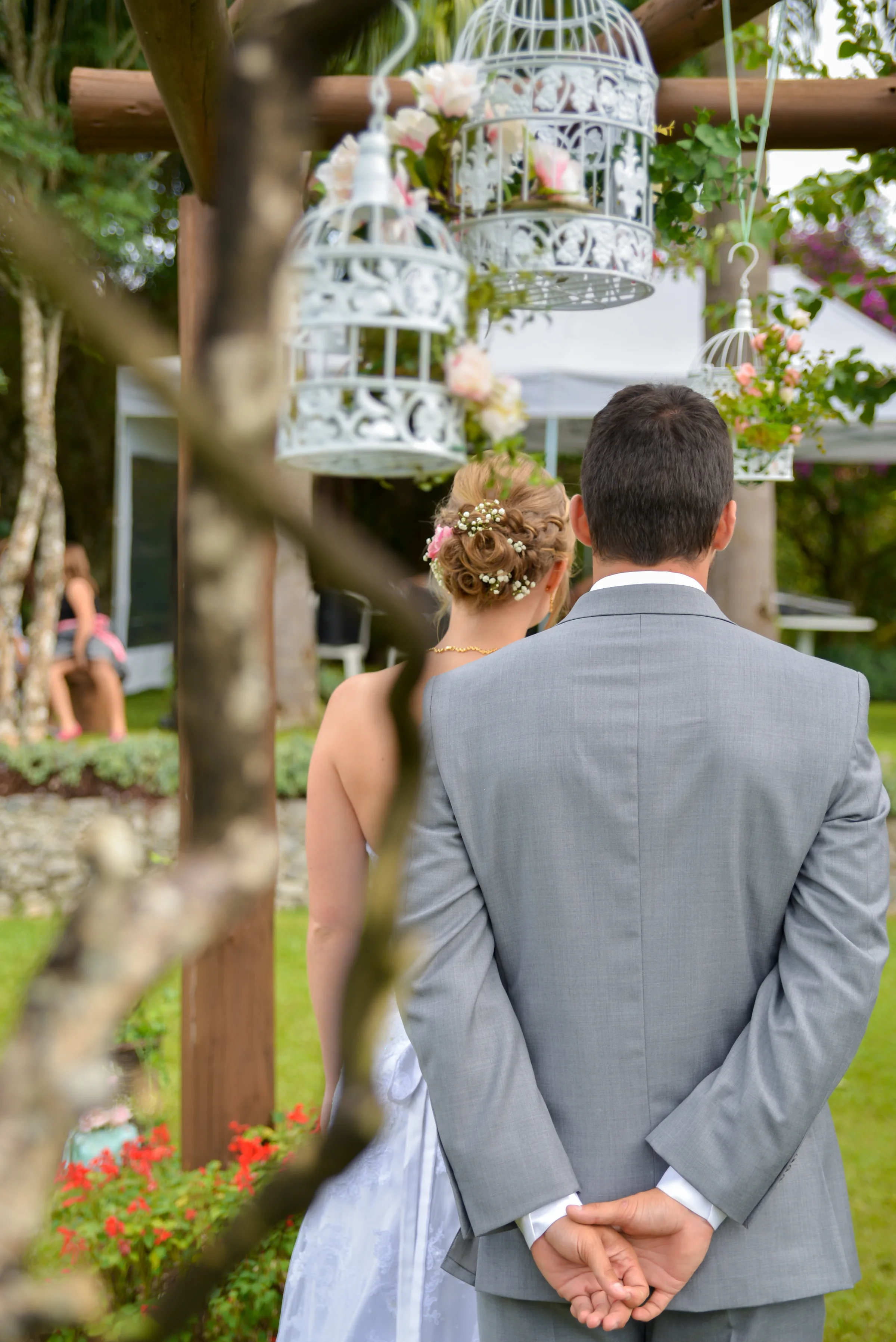 Casal de costas sob gaiolas brancas floridas penduradas no altar do jardim