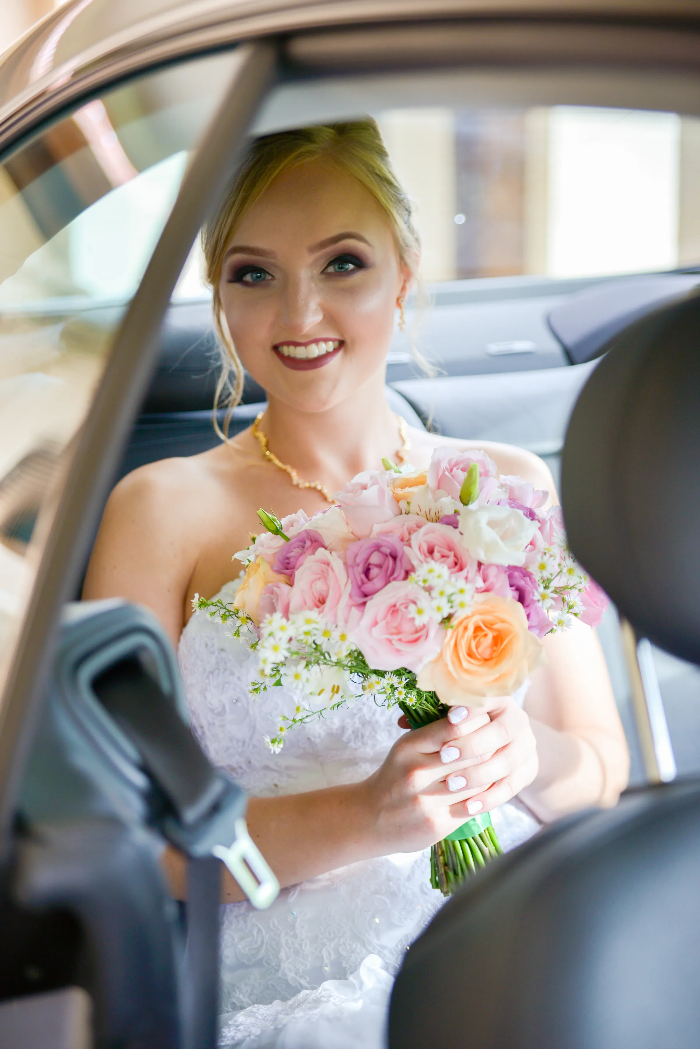Noiva sentada no carro segurando buquê de rosas cor-de-rosa e margaridas