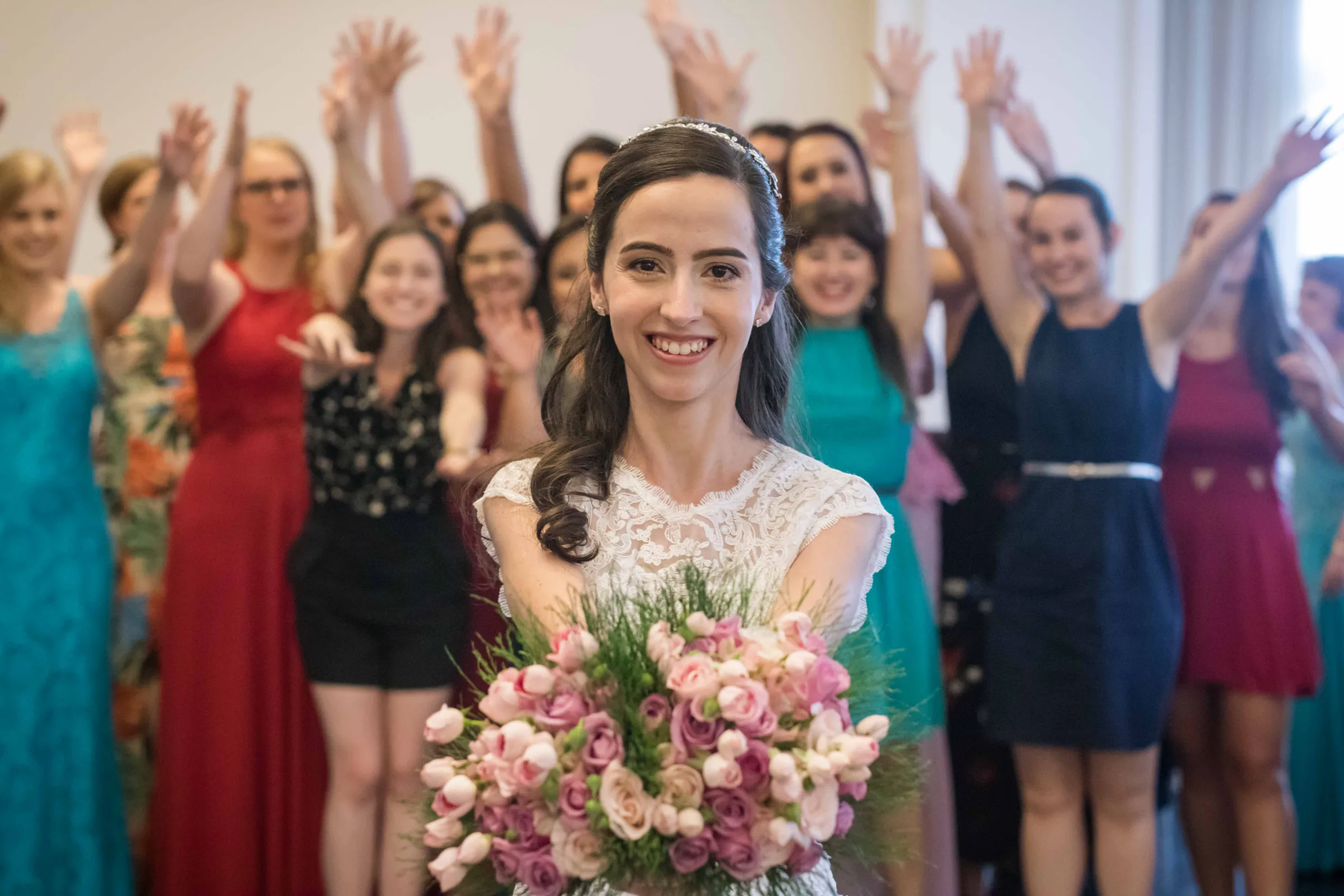 Noiva sorri com buquê de rosas enquanto convidadas erguem os braços atrás