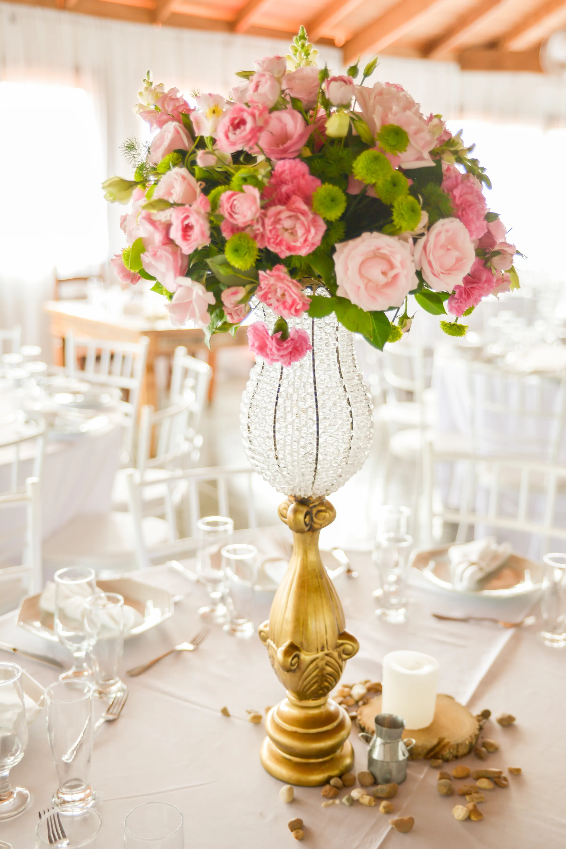 Centro de mesa com rosas cor-de-rosa em vaso dourado e cristais, taças ao redor