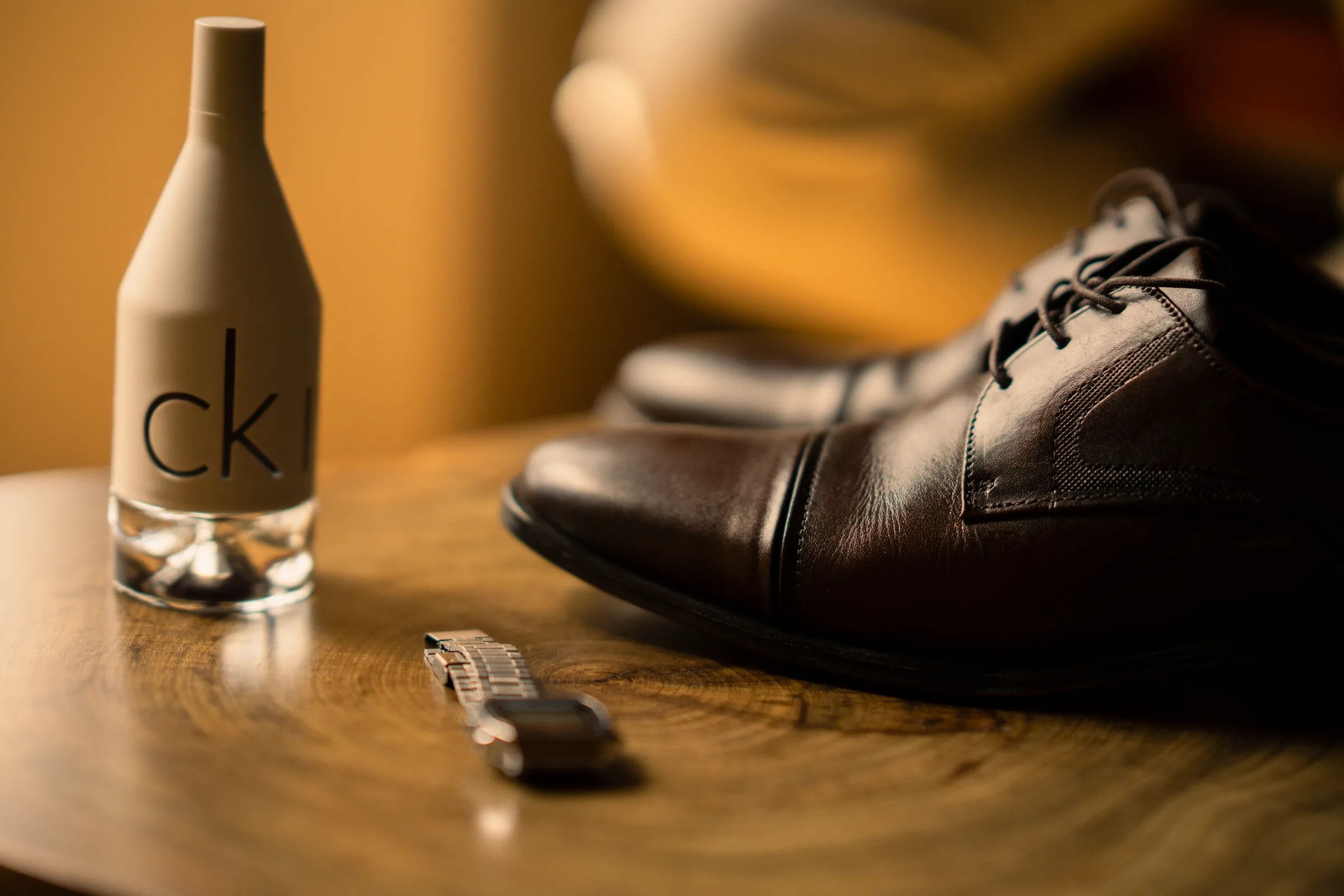 Sapatos marrons, relógio e frasco de perfume sobre mesa redonda de madeira