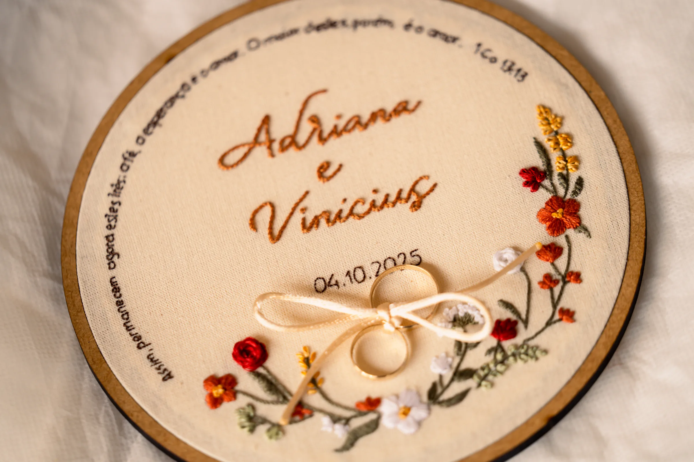 Alianças douradas em bastidor bordado com nomes, data e flores coloridas