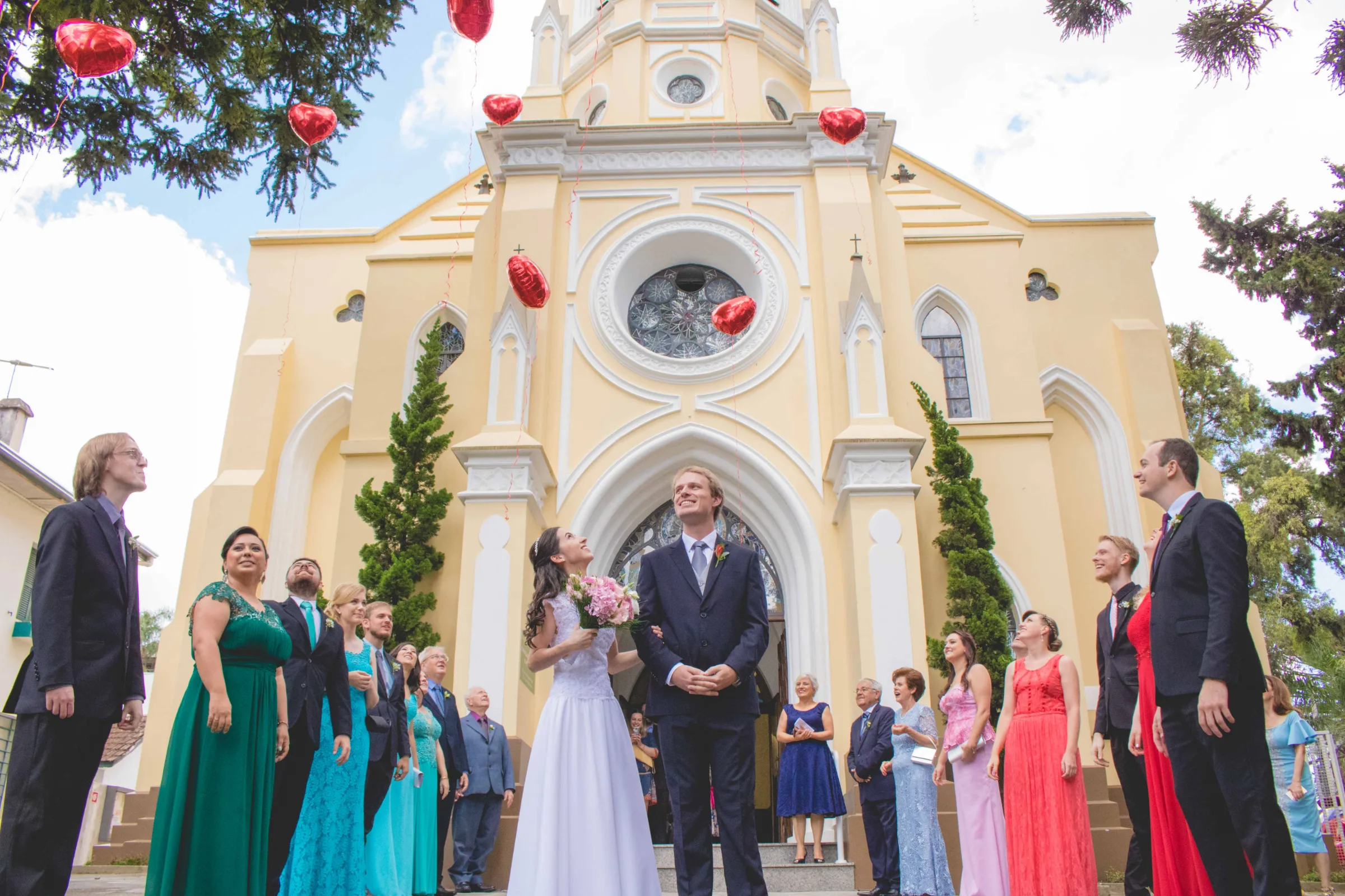 Todos olham para cima acompanhando os balões diante da igreja neogótica