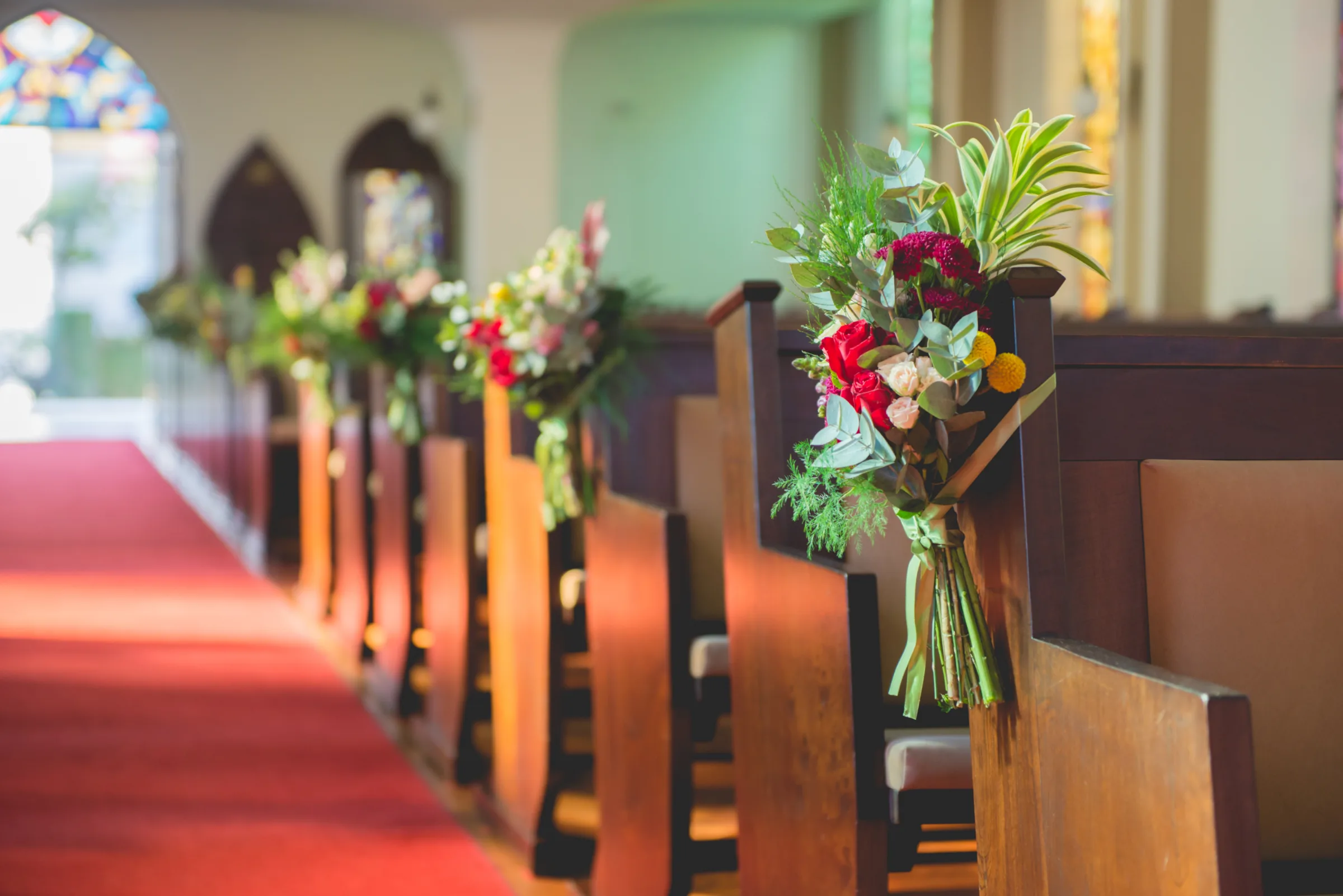 Arranjos de flores presos aos bancos da igreja ao longo do corredor
