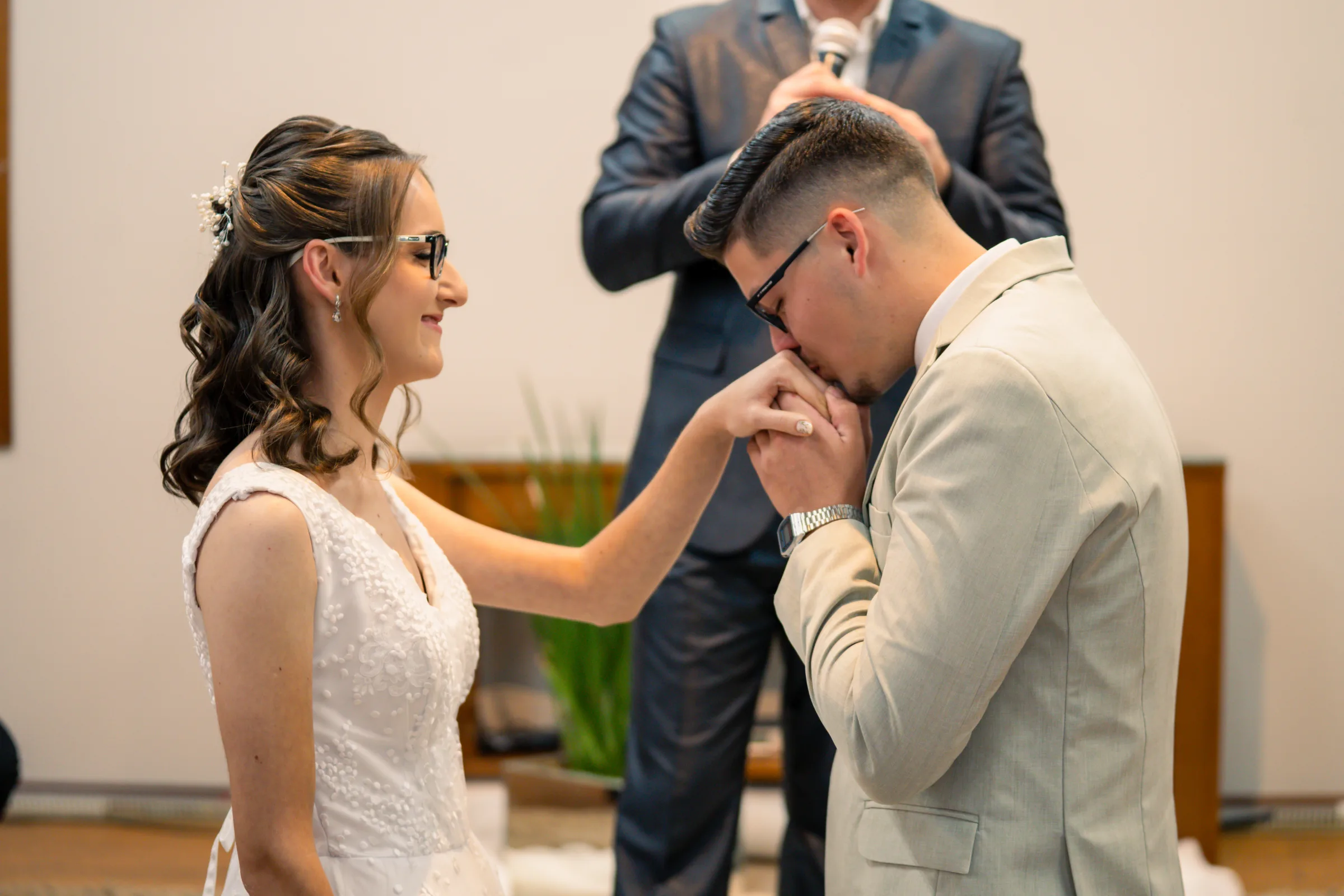 Noivo de terno claro beija a mão da noiva enquanto o celebrante fala