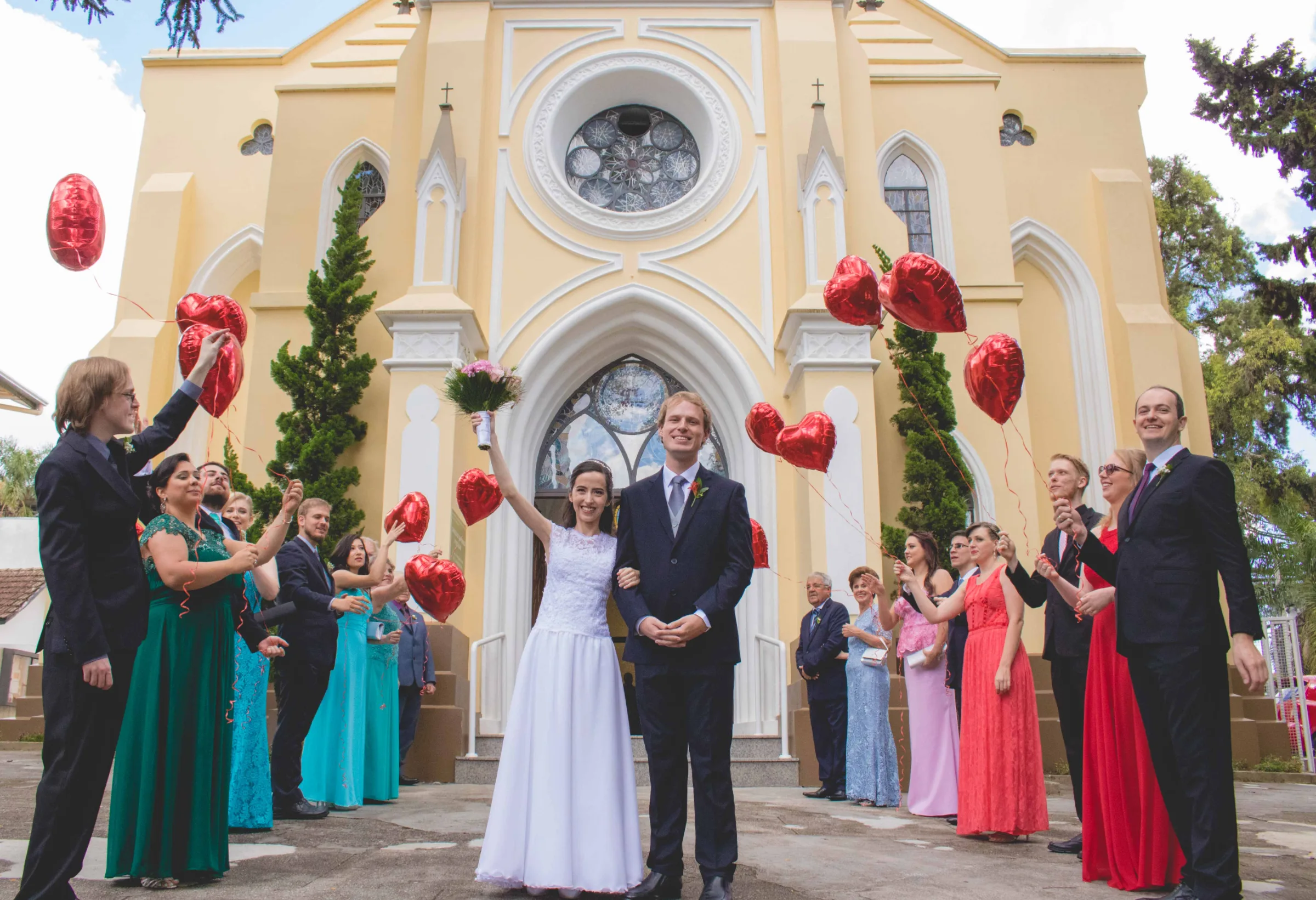 Casal na saída da igreja entre convidados soltando balões vermelhos de coração