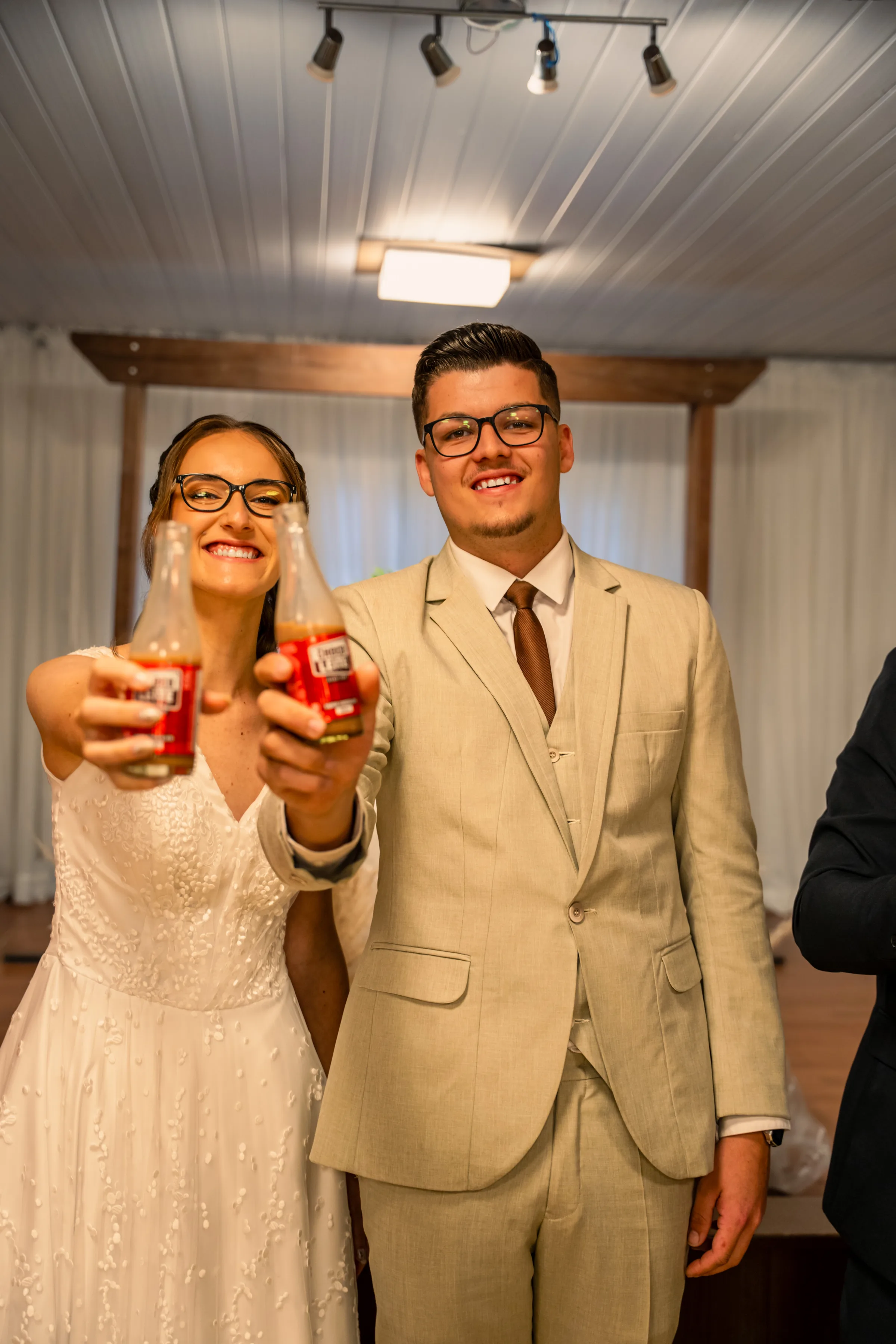 Casal de óculos estende garrafas de refrigerante para a câmera no salão da festa