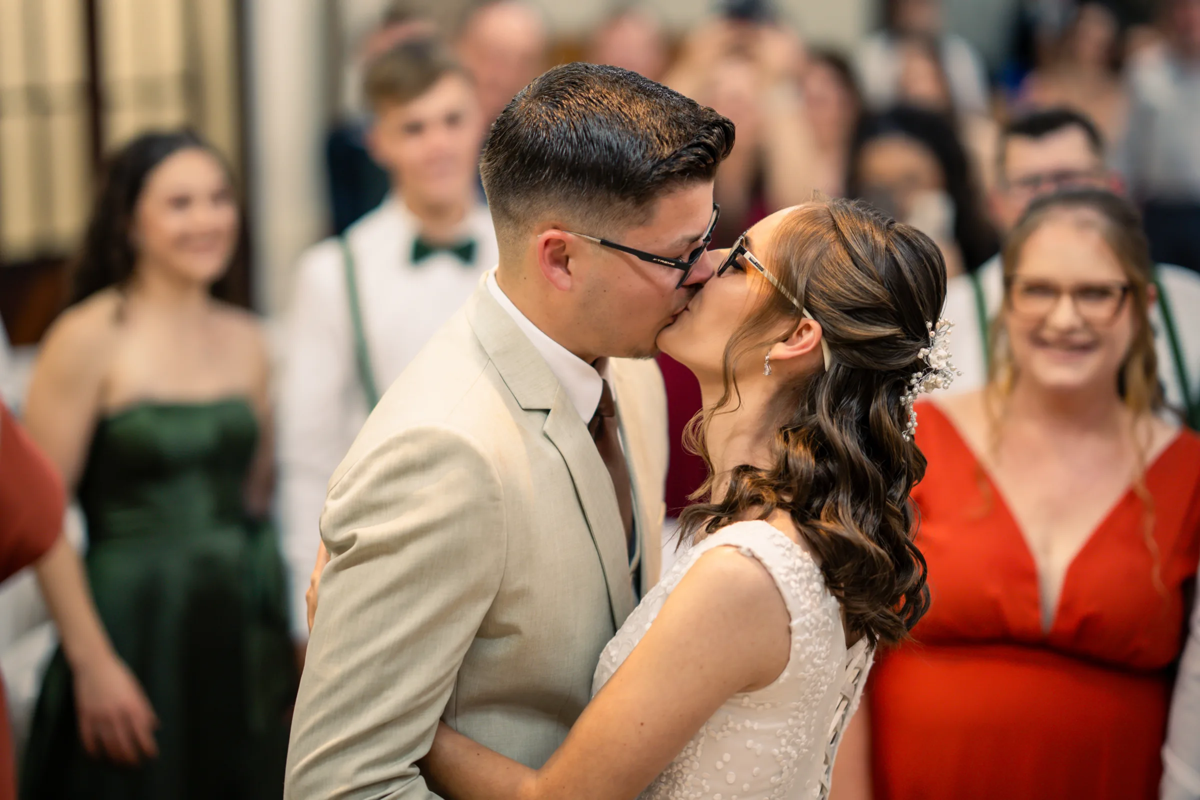 Beijo do casal de óculos diante de padrinhos de verde e convidados