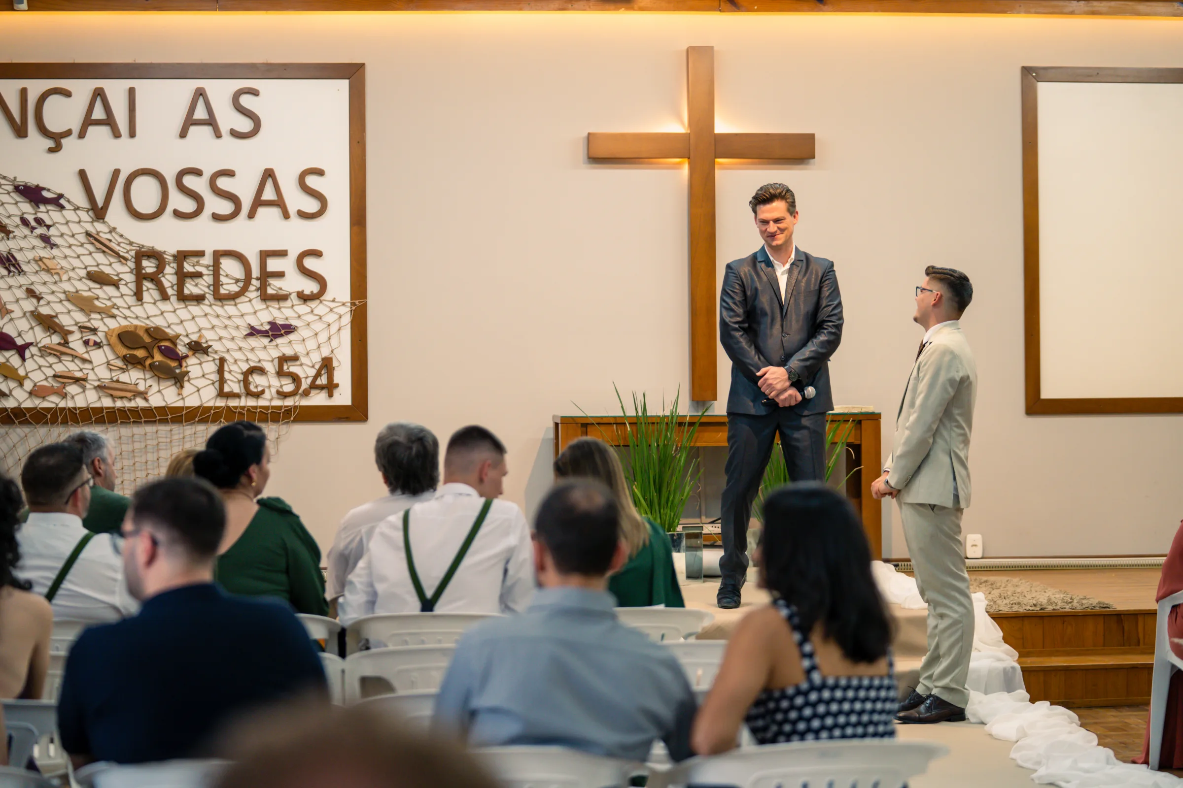 Celebrante e noivo junto à cruz de madeira aguardando diante dos convidados