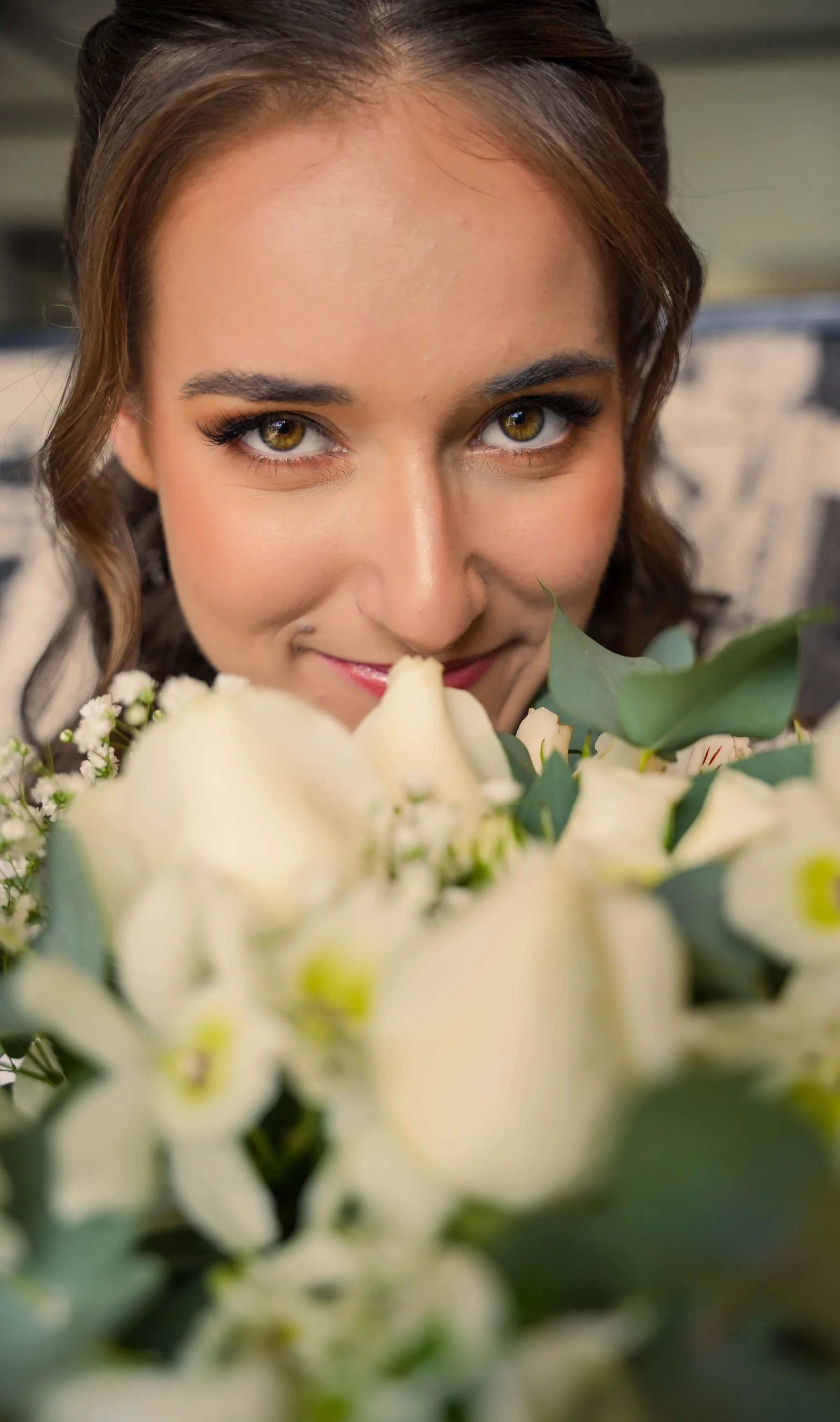 Olhos da noiva aparecendo acima de buquê de rosas brancas e eucalipto
